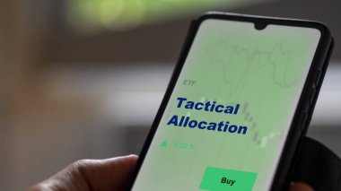Ekrandaki taktik tahsis fonunu analiz eden bir yatırımcı. Bir telefon taktik tahsisat fiyatlarını gösterir