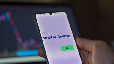 Bir yatırımcı ekrandaki dijital varlıkları analiz ediyor. Bir telefon Dijital Varlıkların fiyatlarını gösterir