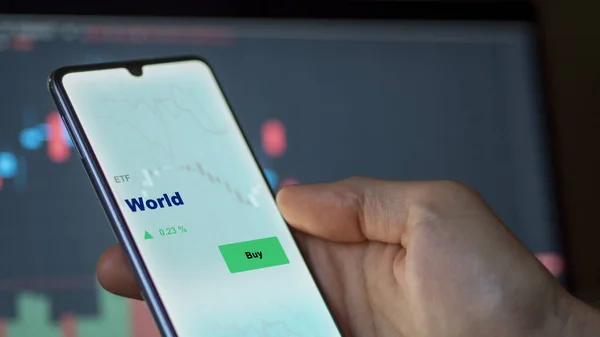stock image An investor analyzing the world etf fund on a screen. A phone shows the prices of World