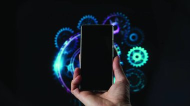 Dijital mekanik ve yapay zekanın arkaplanındaki boş siyah ekranda telefonu önden tutan bir el..