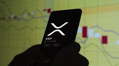 24 Kasım 2023. Telefondaki XRP 'nin fiyatını analiz eden bir yatırımcı. Kripto değiş tokuşunda XRP $..