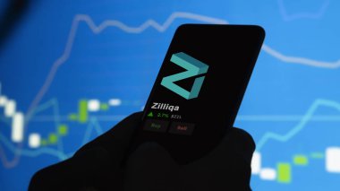 24 Kasım 2023. Telefondaki Zilliqa 'nın fiyatını analiz eden bir yatırımcı. Kripto değiş tokuşu için ZİL $..