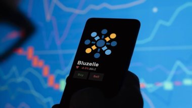 24 Kasım 2023. Telefondaki Bluzelle 'in fiyatını analiz eden bir yatırımcı. Kripto takası için BLZ dolar..