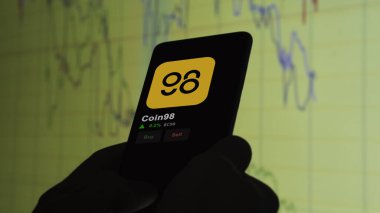 24 Kasım 2023. Telefondaki Coin98 'in fiyatını analiz eden bir yatırımcı. Kripto takası için C98 dolar..