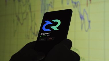 24 Kasım 2023. Telefondaki Decred 'in fiyatını analiz eden bir yatırımcı. Kripto değiş tokuşunda DCR $.