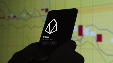 24 Kasım 2023. Bir telefondaki EOS 'un fiyatını analiz eden bir yatırımcı. Kripto değiş tokuşu için EOS $EOS..