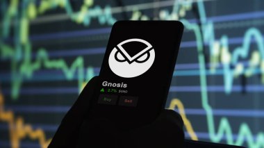 24 Kasım 2023. Telefondaki Gnosis 'in fiyatını analiz eden bir yatırımcı. Kripto takası için GNO $GNO..