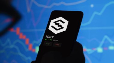 24 Kasım 2023. Bir telefondaki IOST 'un fiyatını analiz eden bir yatırımcı. Kripto değiş tokuşunda IOST $IOST marka para..