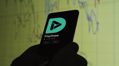 24 Kasım 2023. Telefondaki PlayDapp 'ın fiyatını analiz eden bir yatırımcı. Şifreli bir değiş tokuş için PLA $..