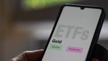 Aralık 2022. Bir yatırımcı telefon ekranı Gold 'daki altın ETF fonunu analiz eder. Almanca çeviri: Kaufen, Verkaufen: al, sat