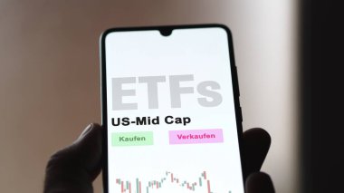 Aralık 2022. Bir yatırımcı, US Mid Cap ETF fonunu telefon ekranında, US-Mid-Cap-ETF 'lerde analiz ediyor. Almanca metin: Kaufen, Verkaufen, US-Mid-Cap alım-satım, US Mid Cap