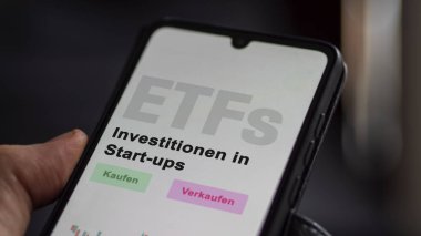 Aralık 2022. Bir yatırımcı, start-up-ETF 'lerdeki ETF fonunun telefon ekranındaki araştırmalarını analiz eder. Almanca metin: Kaufen, Verkaufen, Investitionen in Start-Up 'lar, alım-satım, yatırımlar