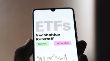 Aralık 2022. Bir yatırımcı, telefon ekranı Nachhaltige Rohstoff-ETF 'de sürdürülebilir hammadde ETF fonunu analiz eder. Almanca metin: Kaufen, Verkaufen, Nachhaltige Rohstoff satın al, sat, sürdürülebilir ham madde