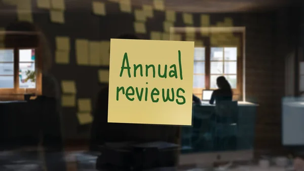 Note with \'Annual reviews\' written on it, in a blurry office background.