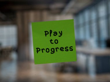 Post note on glass with 'Play to Progress'. clipart