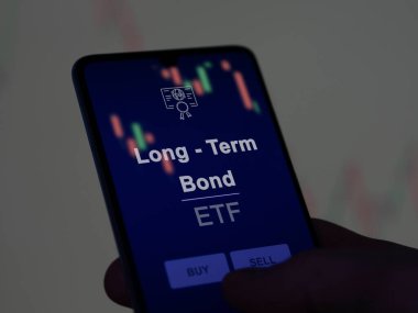 Ekrandaki uzun vadeli tahvil fonunu analiz eden bir yatırımcı. Uzun vadeli tahvillerin fiyatlarını gösteren bir telefon