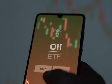 Bir yatırımcı, ekranda petrol fonunu analiz ediyor. Bir telefon petrol fiyatlarını gösterir