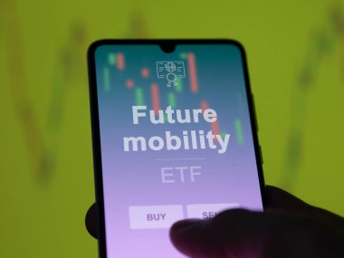 Bir yatırımcı ekranda gelecekteki hareketlilik fonunu analiz ediyor. Bir telefon gelecekteki taşınabilirliğin fiyatlarını gösterir
