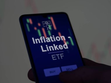 Enflasyonu analiz eden bir yatırımcı. Ekrandaki etf fonu ile bağlantılı. Bir telefon enflasyon fiyatlarını gösterir - bağlantılı