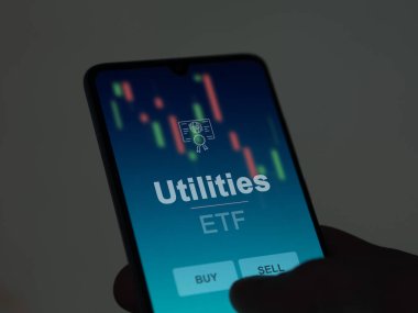 Ekrandaki kamu hizmetleri fonunu analiz eden bir yatırımcı. Bir telefon, hizmetlerin fiyatlarını gösterir