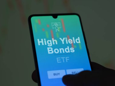 Ekrandaki yüksek gelirli tahvilleri analiz eden bir yatırımcı. Bir telefon yüksek gelirli tahvillerin fiyatlarını gösterir