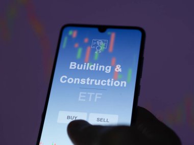 Bir yatırımcı ekranda bina ve inşaat fonunu analiz ediyor. Bina & İnşaat fiyatlarını gösteren bir telefon