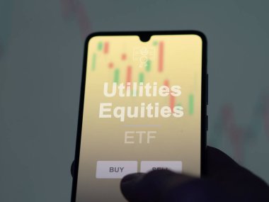 Bir yatırımcı ekrandaki kamu hizmetleri sermaye fonunu analiz ediyor. Bir telefon kamu hizmetleri varlıklarının fiyatlarını gösterir