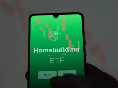 Ekranda ev inşa fonunu analiz eden bir yatırımcı. Ev binasının fiyatlarını gösteren bir telefon