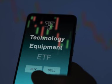 Bir yatırımcı ekrandaki teknoloji ekipman fonunu analiz ediyor. Teknoloji Malzemeleri 'nin fiyatlarını gösteren bir telefon
