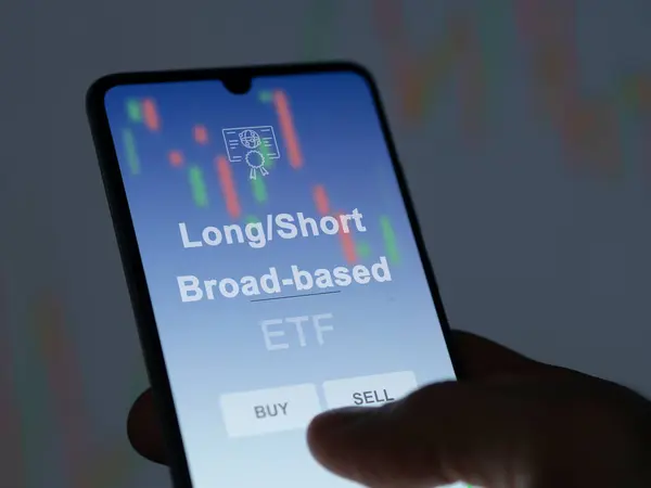 stock image An investor analyzing the long/short broad-based etf fund on a screen. A phone shows the prices of Long/Short Broad-based