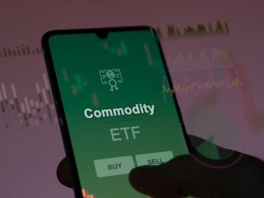 Ekrandaki emtia fonunu analiz eden bir yatırımcı. Bir telefon emtianın fiyatlarını gösterir
