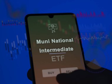 An investor analyzing the muni national intermediate etf fund on a screen. A phone shows the prices of Muni National Intermediate