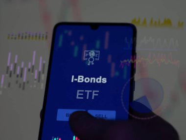Ekrandaki i-bonoları analiz eden bir yatırımcı. Bir telefon I-Bonds fiyatlarını gösterir