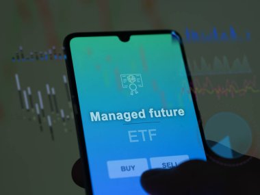 Bir yatırımcı, yönetilen gelecekteki ETF fonunu ekranda analiz ediyor. Bir telefon yönetilen geleceğin fiyatlarını gösterir