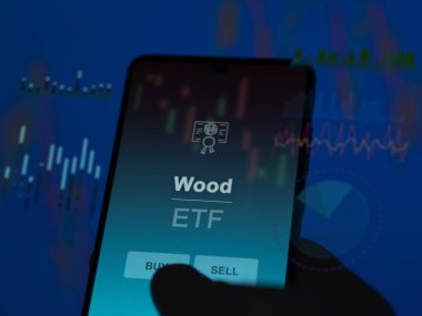 Bir yatırımcı ekrandaki odun fonunu analiz ediyor. Bir telefon ahşap fiyatlarını gösterir