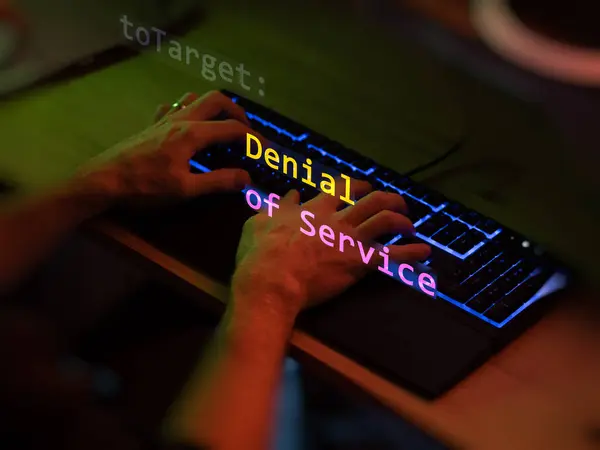 stock image Cyber attack denial of service text in foreground screen, hands of a anonymous hacker on a led keyboard. Vulnerability text in informatic system style, code on editor screen. Text in English, English text