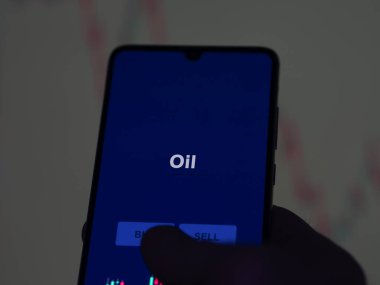 Bir yatırımcı, ekranda petrol fonunu analiz ediyor. Bir telefon petrol fiyatlarını gösterir