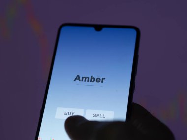 Ekrandaki kehribar fonunu analiz eden bir yatırımcı. Amber 'ın fiyatlarını gösteren bir telefon.