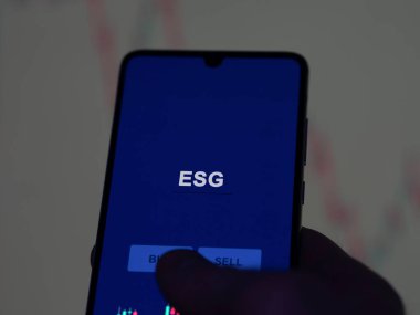 Ekranda ESG fonunu analiz eden bir yatırımcı. ESG 'nin fiyatlarını gösteren bir telefon