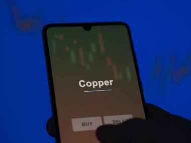 Ekrandaki bakır etf fonunu analiz eden bir yatırımcı. Bakır fiyatlarını gösteren bir telefon.