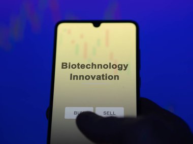 Bir yatırımcı ekrandaki biyoteknoloji yenilik fonunu analiz ediyor. Biyoteknoloji İnovasyonunun fiyatlarını gösteren bir telefon