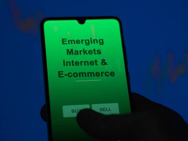 Gelişmekte olan piyasaları analiz eden bir yatırımcı bir ekranda internet ve e-ticaret etf fonu. Bir telefon, Gelişmekte Olan Piyasaların İnternet & E-ticaretinin fiyatlarını gösterir