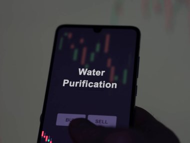 Ekrandaki su arıtma fonunu analiz eden bir yatırımcı. Bir telefon su arıtma fiyatlarını gösterir