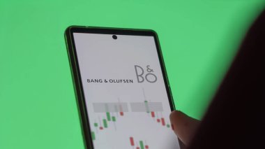 Ekranda Bang & olufsen etf fonunu analiz eden bir yatırımcı. Bang & Olufsen fiyatlarını gösteren bir telefon