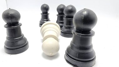 Tehdit konsepti, zorbalık konsepti, beyaz satranç taşları, siyah satranç taşları kalabalığından diz çöküp düşme, Asya Endonezya