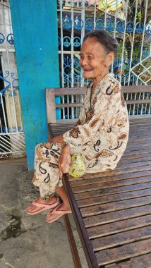 Pinrang Endonezya 28 Temmuz 2023: Yaşlı bir anne, Masolo Pinrang Endonezya köyünde sağlıklı ve mutlu bir gülümsemeyle salonda rahat bir şekilde oturuyor.