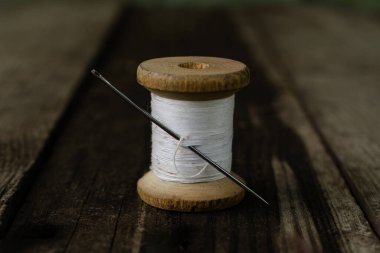 Beyaz iplikli bir bobbin ve içinde siyah iplik olan bir iğne tahta bir masanın üzerinde duruyor. Dikiş ve dikiş ipliği, eski makara ipliği