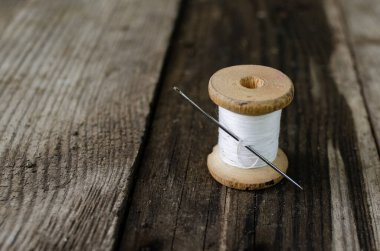 Beyaz iplikli bir bobbin ve içinde siyah iplik olan bir iğne tahta bir masanın üzerinde duruyor. Dikiş ve dikiş ipliği, eski makara ipliği
