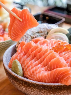 Sashimi hazırla. Çiğ somonu yemek masasındaki bir kaseye koy. Somon, yemek çubuklarıyla alınıyor. Kase wasabi, zencefil, limon ve limonla süslenmiş..