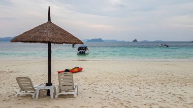 Plaj sandalyeleri, şemsiyeler, kumsalda kayıklar, denize bakan kayıklar, adaya bakan sürat tekneleri ya da yatlar Myanmar 'daki bir adada yaşayan kalabalık olmayan insanlar.